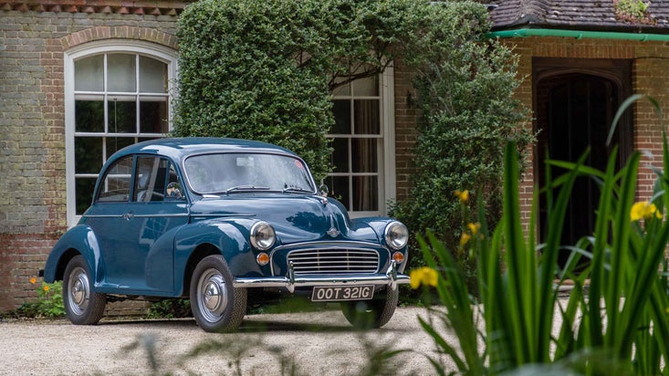 A blue Morris Minor car parked outside the front of Nuffield Place